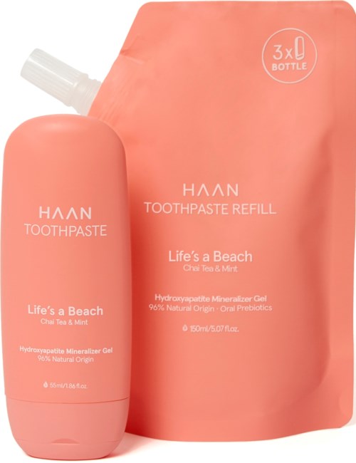 Eine rosa Zahnpastaflasche und Nachfüllpackung mit orangefarbiger Verpackung, beschriftet 'Life's a Beach' mit Chai Tee und Minzgeruch.