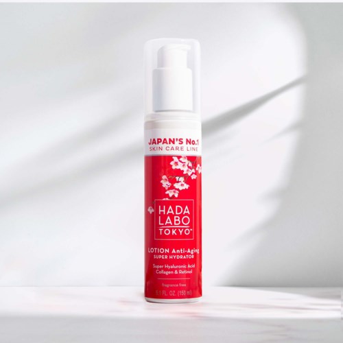 Punainen ja valkoinen pullo Hada Labo Tokyo anti-aging voiteesta, jossa kirsikankukkakuva etikettissä.