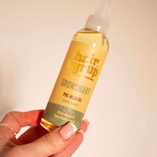 Een kleine fles met de tekst 'haarserum' vastgehouden door een hand. De fles is geel en grijs.