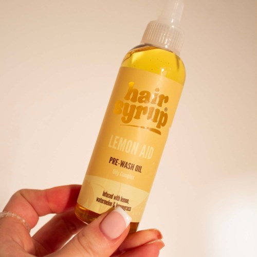 Kleine gele fles met spraydop, gemarkeerd 'hair syrup', bevat pre-wash olie met citroengeur.
