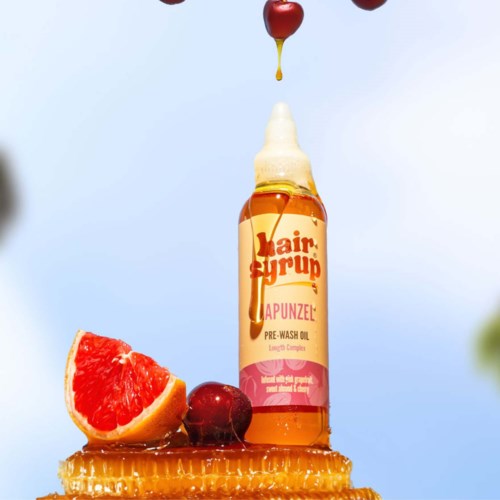 A hair syrup bottle is surrounded by grapefruit, cherry, honeycomb, and drops falling from above.