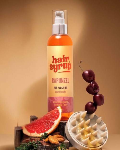 Een fles haarserum, kersen, grapefruitpartje, noten en een huidverzorgingsgereedschap worden getoond.
