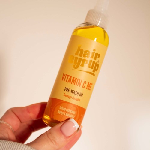 Een hand houdt een fles haarserum met gele vloeistof genaamd Vitamin C pre-wash olie.