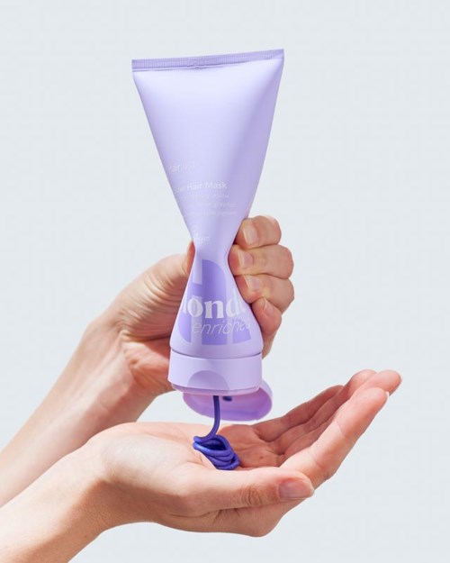 A hand holding a lavender tube of hair mask with some product squeezed out.