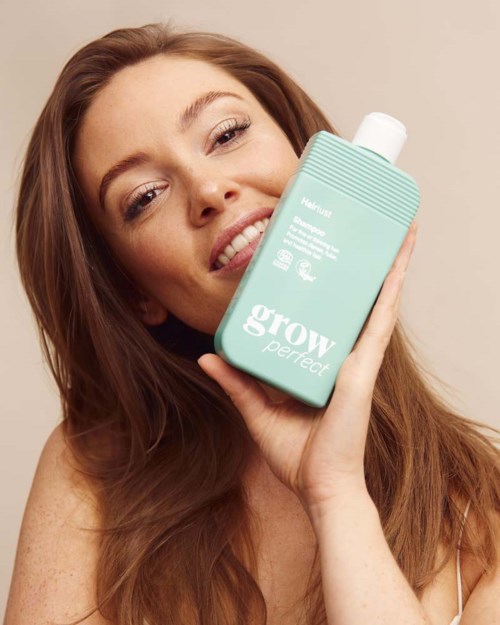 A smiling woman with long, wavy hair holds a turquoise bottle labeled grow perfect skincare.