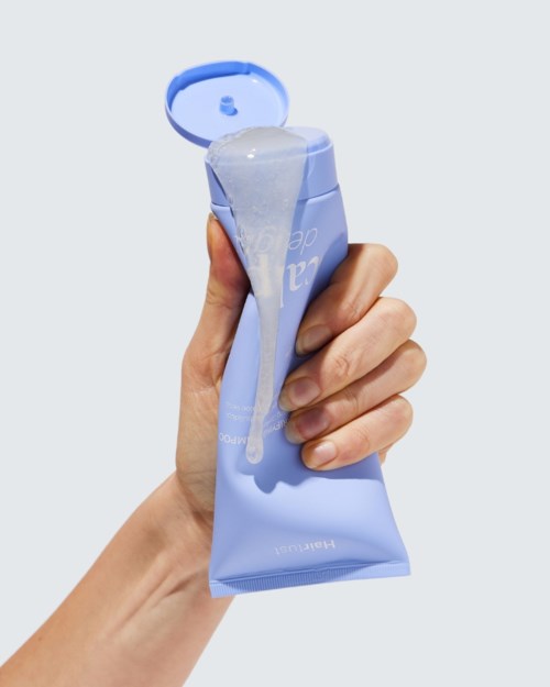 Hand som pressar ut en blå tub med hudvårdsprodukt med kräm som kommer ut.