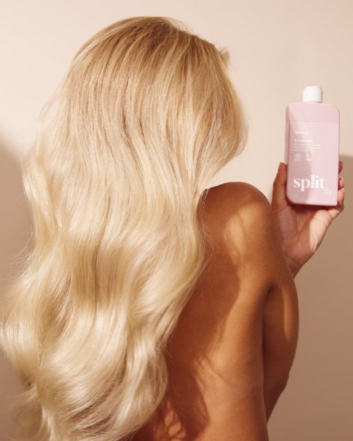 Blonde woman with wavy hair holds pink bottle with white cap, the label says split.