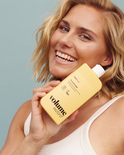 Smiling woman holding a yellow bottle of hair care product labeled Volume Wizardo.