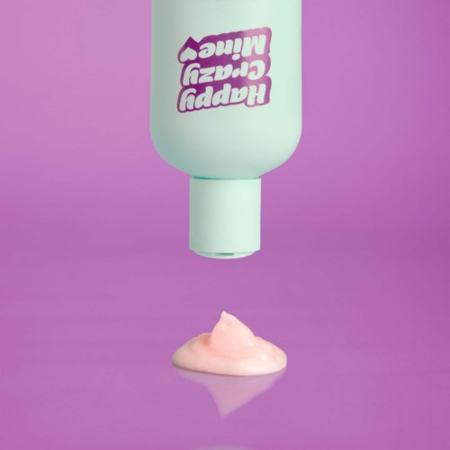 Een flesje met de tekst "Happy Crazy Cream" hangt ondersteboven en druppelt roze room op een paarse ondergrond.