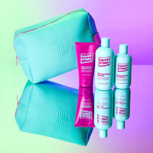 Drie flessen en een tube schoonheidsproducten in roze en wit met een turquoise tas, weerkaatst op een glanzend oppervlak.