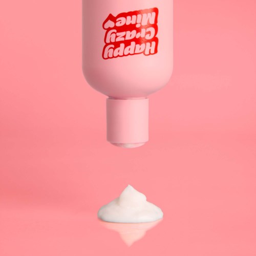 Een roze fles met rode tekst die witte schuim uitscheidt op een roze achtergrond.