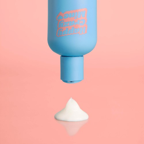 Een blauwe flesje met 'happy bubble wind' erop is ondersteboven met schuim dat eruit komt op een roze achtergrond.