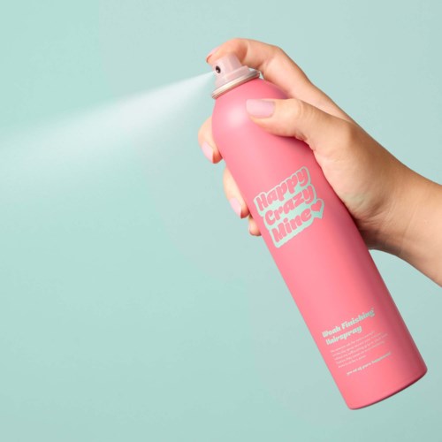 Een hand spuit een roze bus met 'Happy Crazy Mine' erop tegen een lichtblauwe achtergrond.