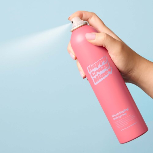 A hand sprays a pink bottle labeled "Happy Creamy Time" with white mist inside a light blue background.