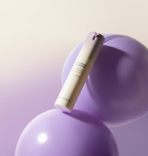 A white cylindrical bottle placed on two purple balloons, with a light purple background.