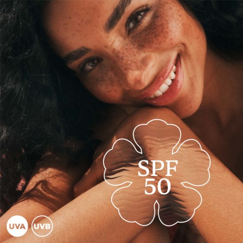 Een lachende vrouw met sproeten toont haar gezicht en arm met SPF 50 zonnebrandbescherming symbolen. Achtergrond is donker.