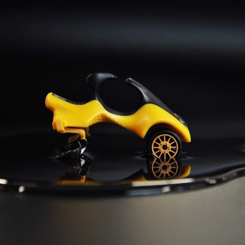 Ein kleiner Spielzeugwagen in Gelb und Schwarz mit einzigartigem Design steht auf einer dunklen spiegelnden Oberfläche.