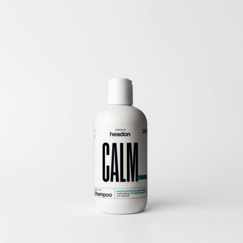 Een witte shampoo fles met zwarte en teal tekst, met het label Calm en Headon, staat alleen op een witte achtergrond.
