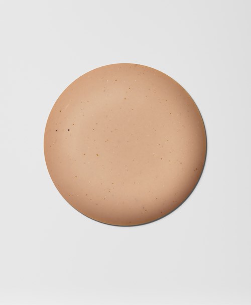 Pyöreä, beige esine, jossa on pieniä tummia pisteitä, vaaleanharmaalla taustalla.