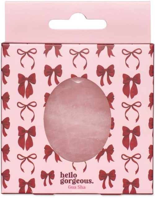 Lyserosa gaveeske med røde sløyfemønster og et gjennomsiktig ovalt vindu, merket Hello Gorgeous Gua Sha.