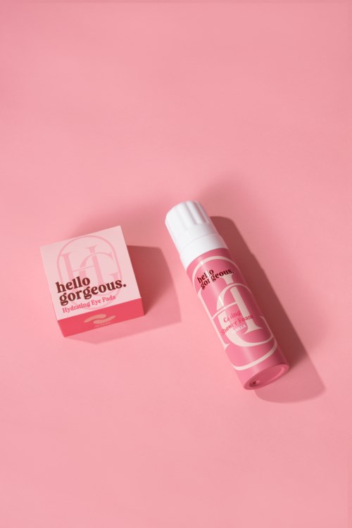 Roze huidverzorgingsproduct met tube en doos, beiden met de tekst "Hello Gorgeous." De achtergrond is roze.