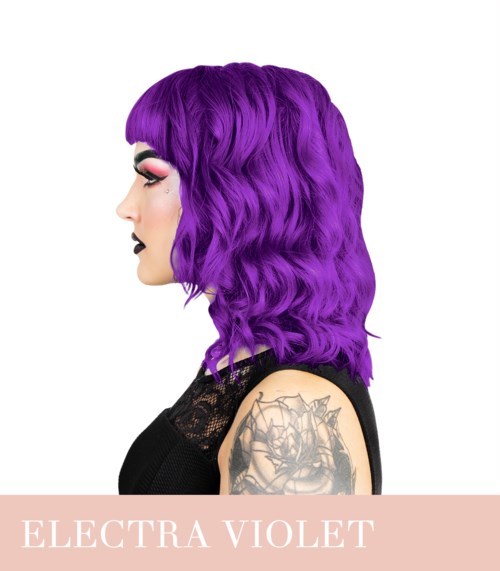 A woman with purple, wavy hair and tattoos on her arm, wearing dark makeup and a black top.