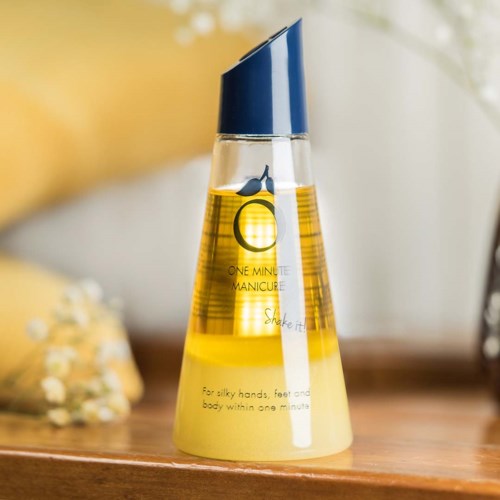 A nail oil bottle with a blue cap, yellow liquid, and a cute whale illustration. It is on a wooden surface.