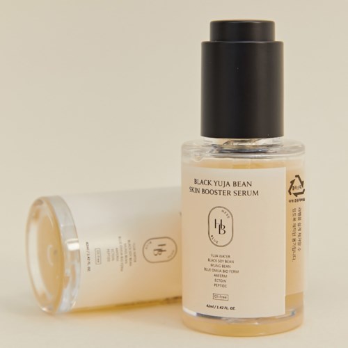 Eine kleine transparente Flasche mit schwarzem Deckel, beschriftet mit Black Yuja Bean Skin Booster Serum, liegt neben einer ähnlichen Flasche.