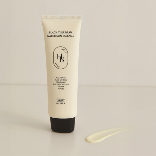Ein weißes Tube mit schwarzem Deckel zeigt ein Hautpflegeprodukt namens Black Yuja Bean Water Sun Essence. Eine kleine Menge ist daneben ausgestoßen.