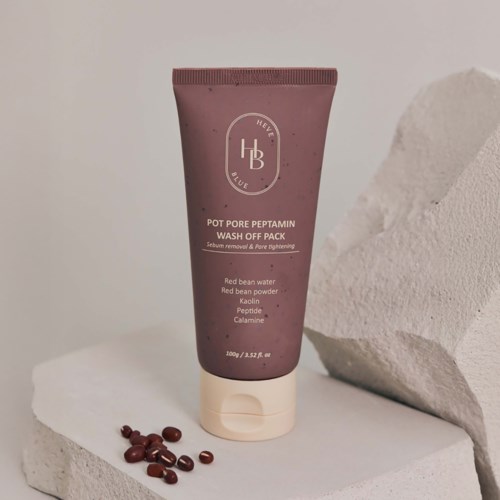 Eine lila Tube mit der Beschriftung 'Pot Pore Peptamin Wash Off Pack' mit Zutatenliste, steht auf weißer Oberfläche mit kleinen roten Bohnen.