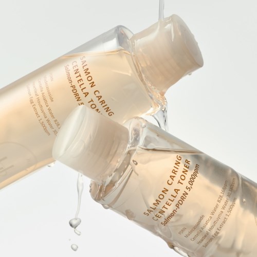 Zwei Hautpflegeflaschen mit Salmon Caring Centella Toner sind gestapelt und tropfen Flüssigkeit.