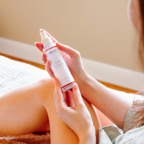 A person applying lotion or cream to their arm using a spray bottle at home.