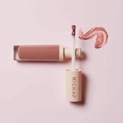 Lip gloss tube and wand with pinkish gloss on a pastel pink background.