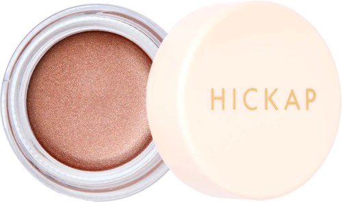 A small round container with beige shimmer eyeshadow and a white lid showing the brand name 'HICKAP' in gold.