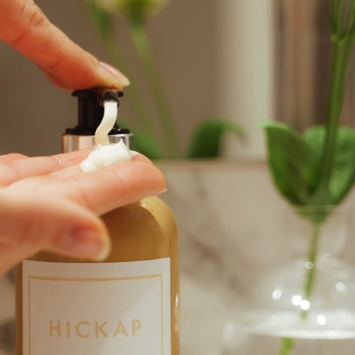 A hand pressing a pump on a soap or lotion bottle in a bathroom or sink area.