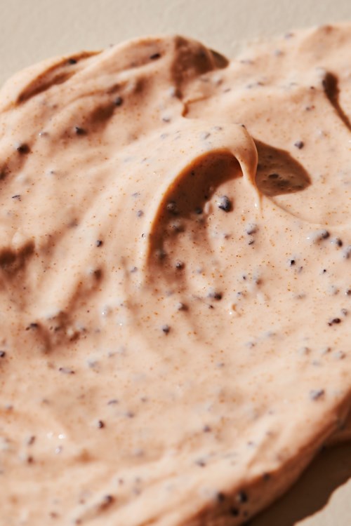 Creamy, speckled spread, possibly peanut butter with chocolate or spice bits. Thick texture and light brown color.