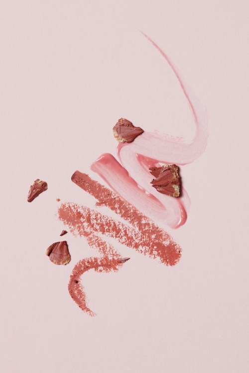 Pink and brown makeup products and scattered powder on a light pink background.