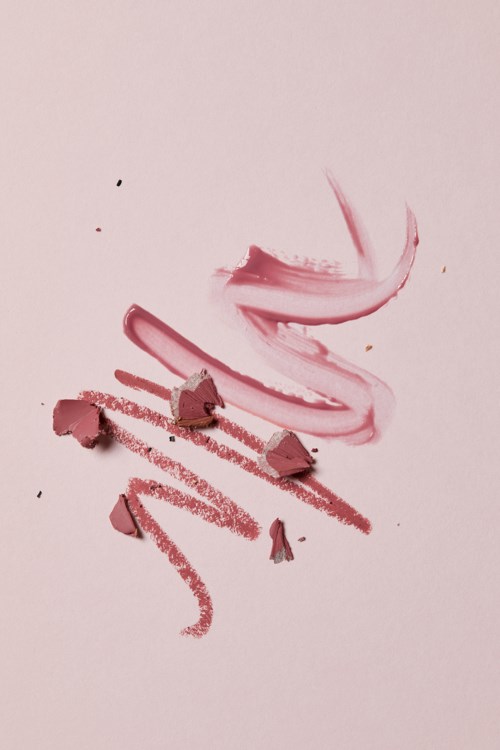 Pink lipstick swatched with broken pieces and smudges on a light background.