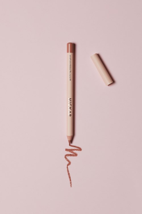 A pink lipstick with its cap placed nearby, drawing a wavy line on pink background.