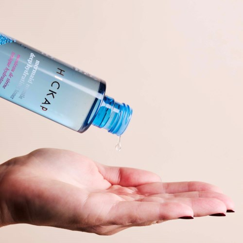 A hand holds out open palm while liquid is poured from a blue plastic bottle.