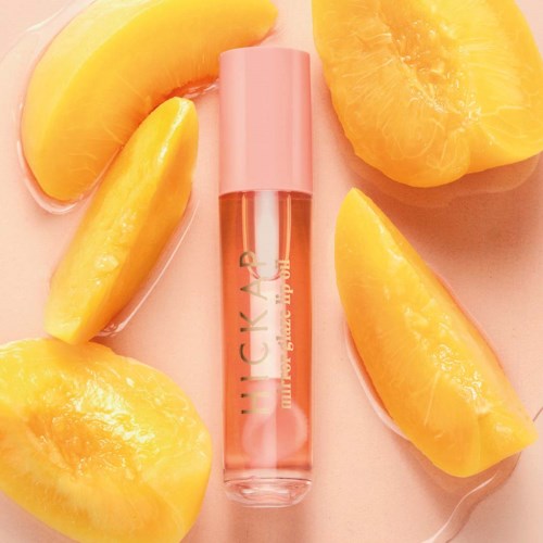 Lip gloss tube surrounded by peach slices, with a pink cap and shiny, clear gloss inside.