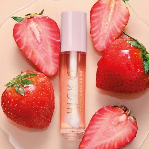 Lip gloss bottle surrounded by fresh strawberries, some halved.