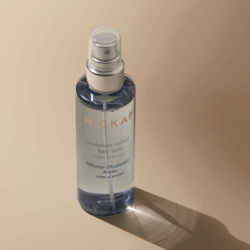 A clear spray bottle with a pump, labeled 'HICKAP', contains a face mist for hydration and calming.