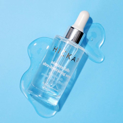 A clear bottle with a white dropper cap, lying on a blue background with some water around.