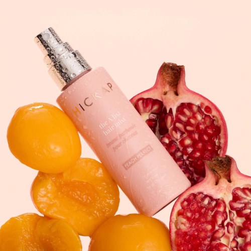 A pink spray bottle labeled 'peach nectar' with pomegranate halves and peaches around it.