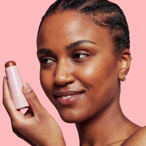 A woman with natural hair uses a small pink device with white text on it against a pink background.