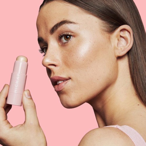 A woman with smooth skin holds a pink skincare product against a pink background.