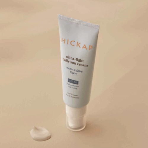 A white tube of sunscreen cream with the brand name 'HICKAP' and SPF 50 written on it, with cream beside it.