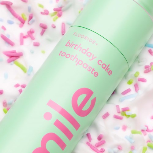 Een pastelgroene buis met de tekst 'birthday cake toothpaste' omgeven door kleurrijke hagelslag op een witte oppervlakte.