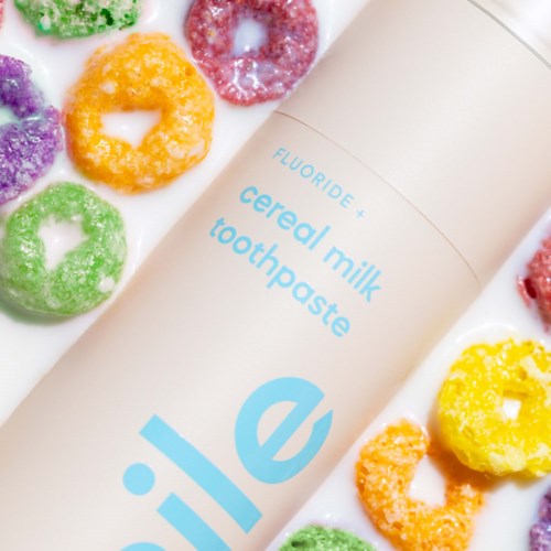 Eine weiße Flasche mit Cereal Milk Zahnpasta umgeben von bunten Cerealien-ähnlichen Süßigkeiten.